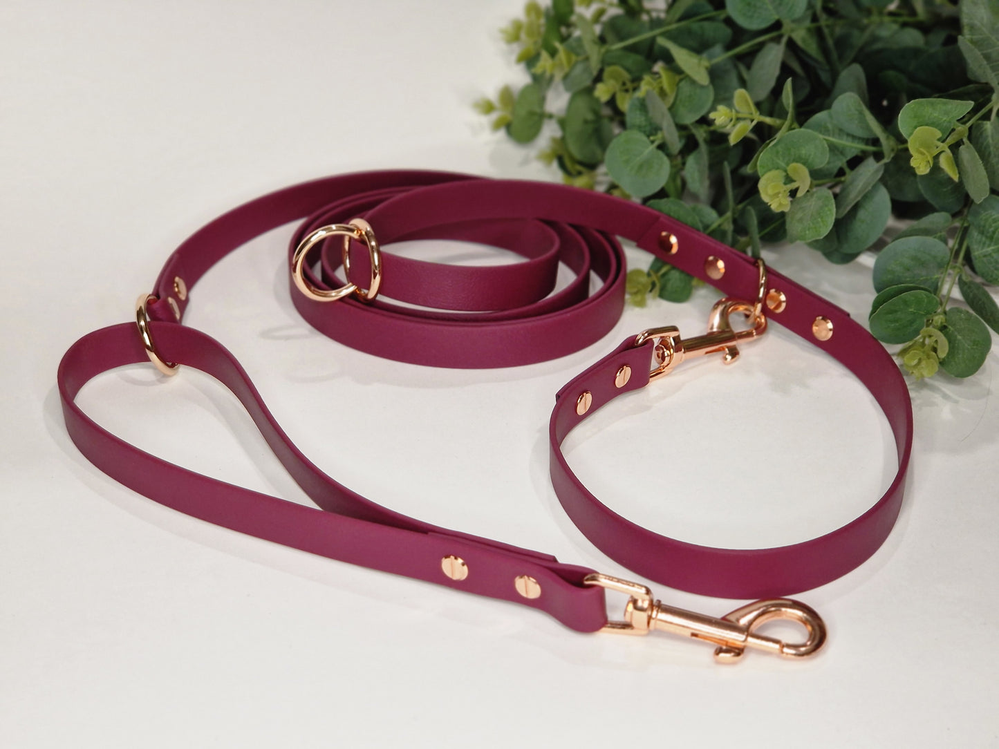 Wine-Colored Biothane Multifunctional Dog Leash with Copper Carabiners, thoughtfully arranged on a background of lush greenery for decoration.