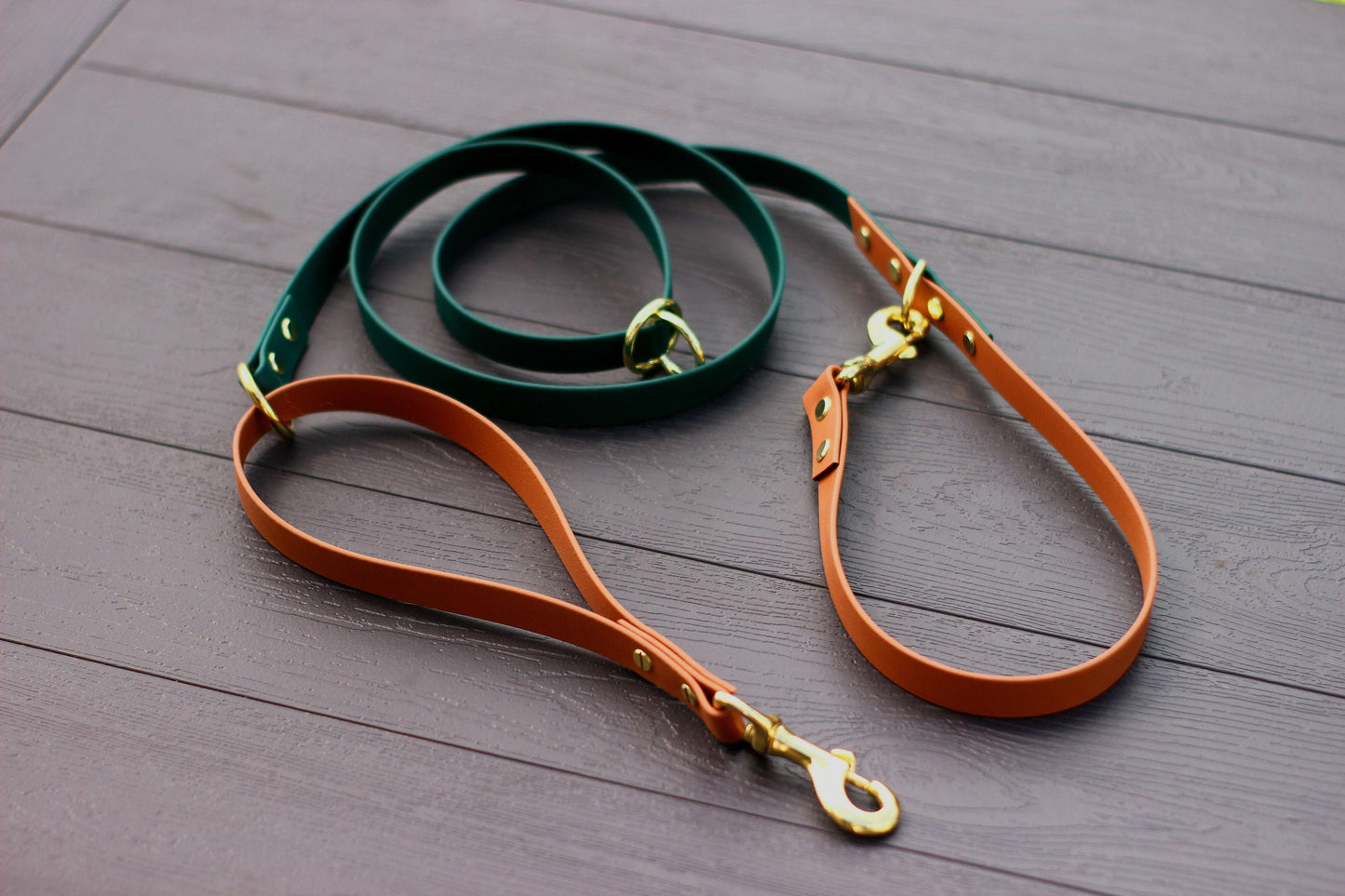 Biothane Multifunctional Dog Leash in Vibrant Orange and Green with Golden Carabiners, elegantly displayed on a wooden surface.